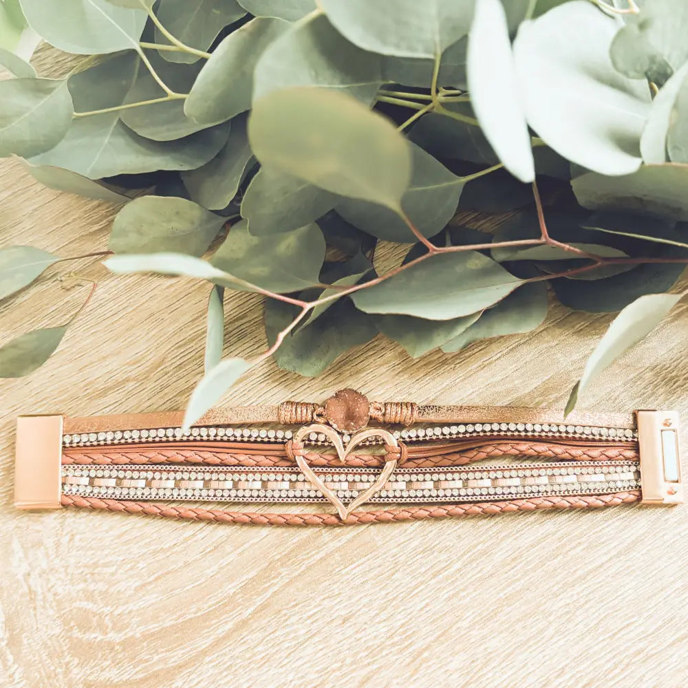 A rose gold heart charm adorns a multi-strand braided leather bracelet with crystals and metallic clasps