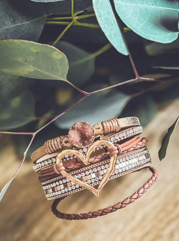 A layered brown leather bracelet set featuring a rose gold braided heart charm and sparkling crystal accents