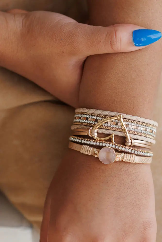 A stack of layered rose quartz and leather bracelets with woven bands and gold-toned metal accents