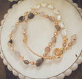 A delicate pearl and crystal beaded gold charm bracelet with translucent white, beige, and smoky gray stones