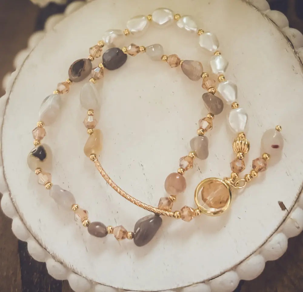 A delicate pearl and crystal beaded gold charm bracelet with translucent white, beige, and smoky gray stones