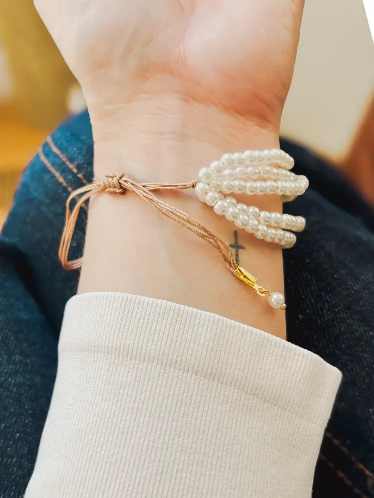 Multi-strand pearl bracelet with beige braided cord and gold-toned clasp showcasing elegant layered design