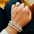 A delicate multi-strand pearl bracelet with evenly sized white beads, braided cord, and gold clasp wrapped around the wrist