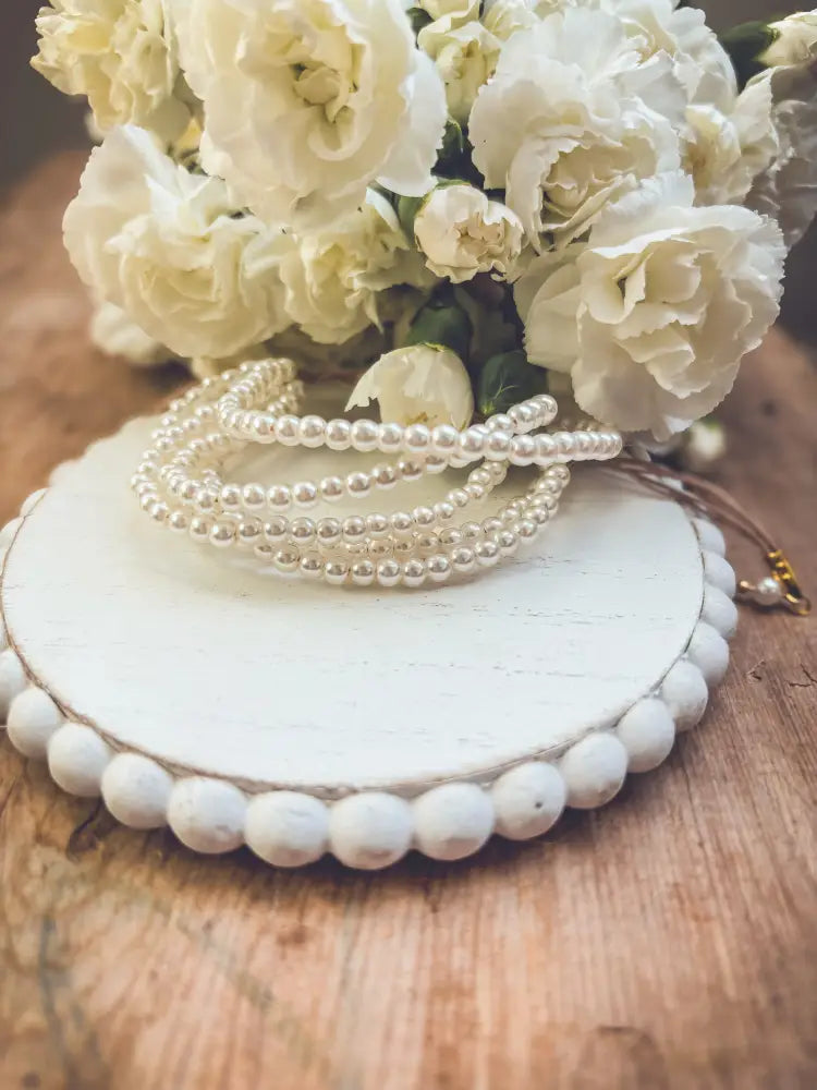 Multi-strand pearl bracelet featuring cream-colored freshwater pearls coiled on rustic white wooden display with gold clasp