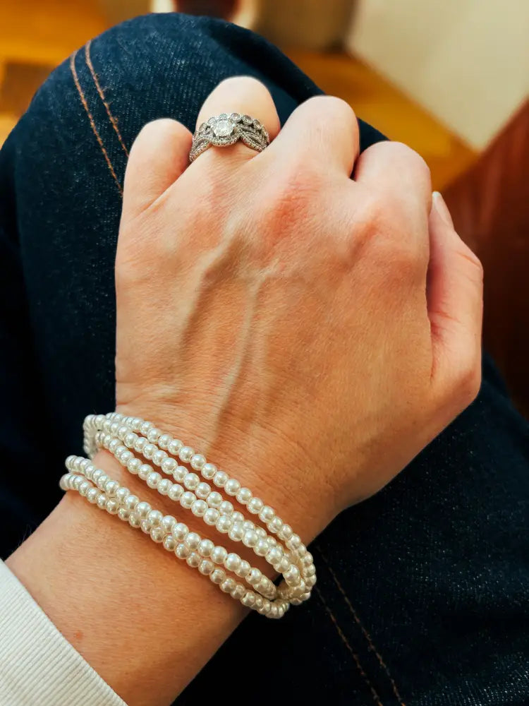 Multi-strand pearl bracelet with braided cord and gold clasp featuring delicate white beads wrapped around wrist