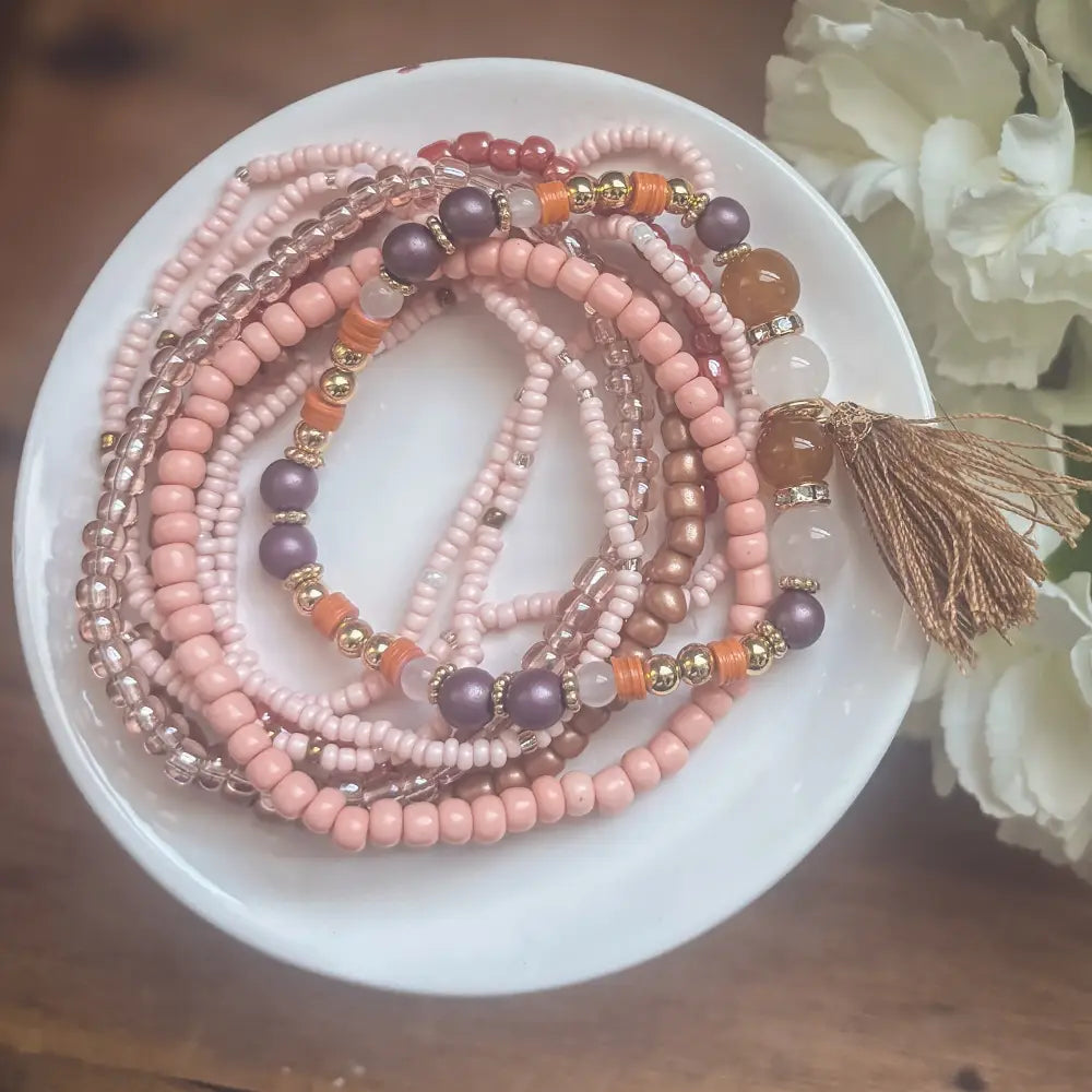 A set of delicate pink mauve and gold-toned beaded stacking bracelets with a matching tassel accent