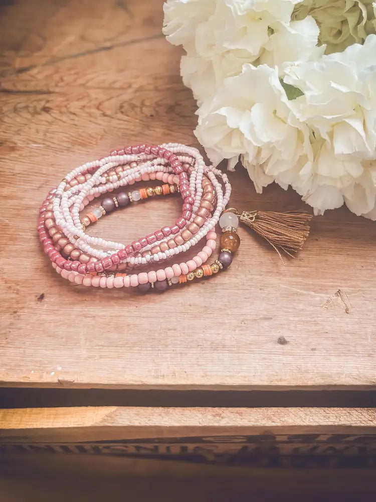 A delicate multi-strand pink and earth tone beaded tassel stacking bracelet set featuring soft pink cream and brown beads