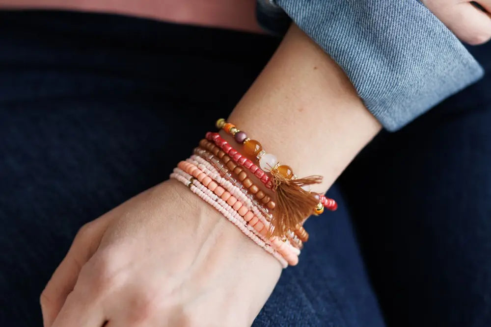 A stack of pink and earth tone beaded bracelets with tassel accents featuring terracotta and amber hues