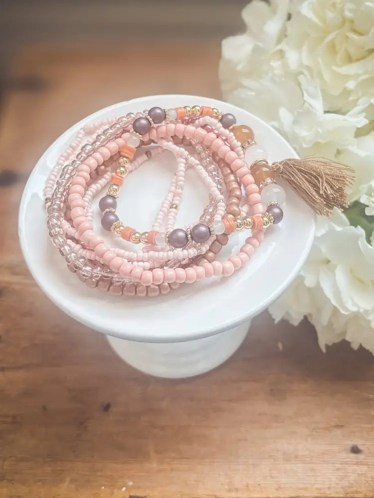 A set of delicate pink and gold beaded stretch bracelets with matching tassel accent for stacking