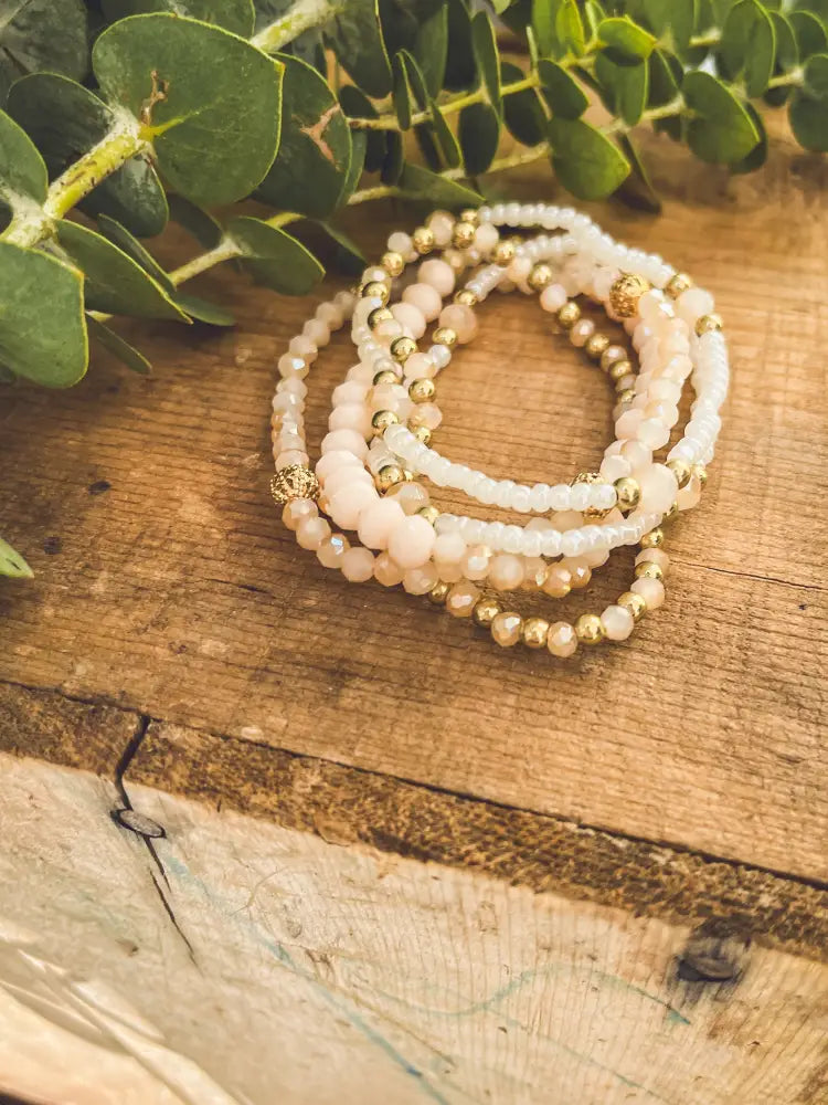A delicate stack of blush pink and gold beaded stretch bracelets with faceted glass beads and metallic accents