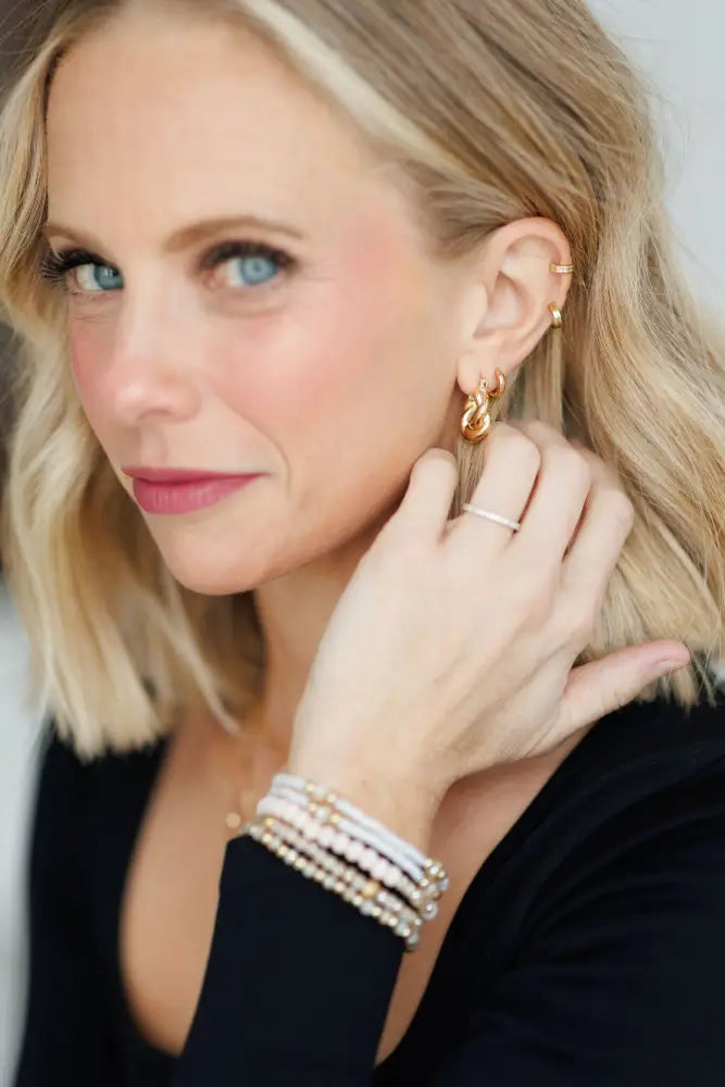 Gold-toned twisted hoop earrings with delicate intricate design paired with elegant pink and gold beaded stacking bracelet set