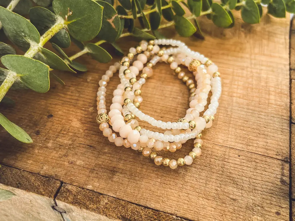 A delicate stack of blush and gold beaded stretch bracelets with faceted glass beads and metallic accents