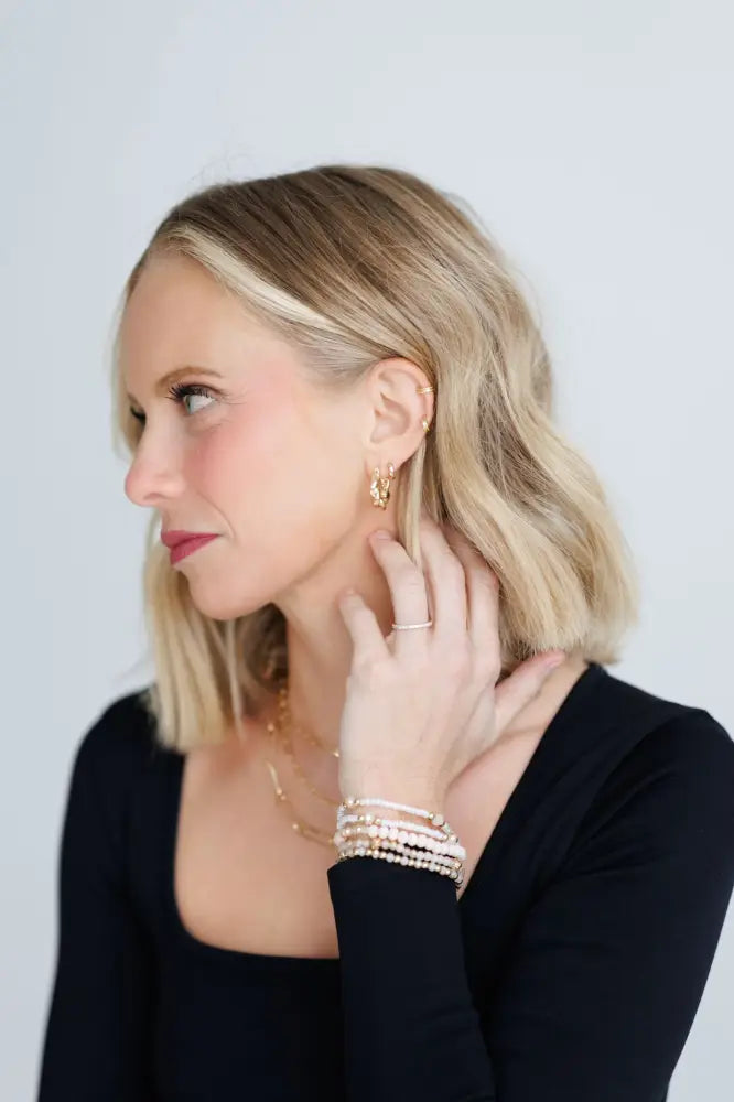 Gold-toned hoop earrings with a delicate textured design paired with elegant pink and gold beaded stacking bracelets