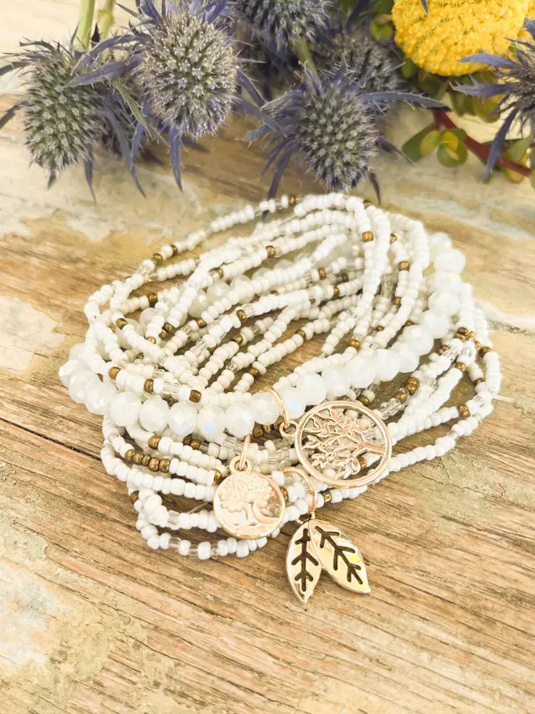 A delicate white and gold tree of life beaded stacking bracelet set featuring multi-strand beads and charms