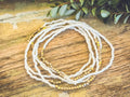 A delicate white and gold beaded multi strand stretch bracelet set featuring smooth cylindrical beads with metallic sheen