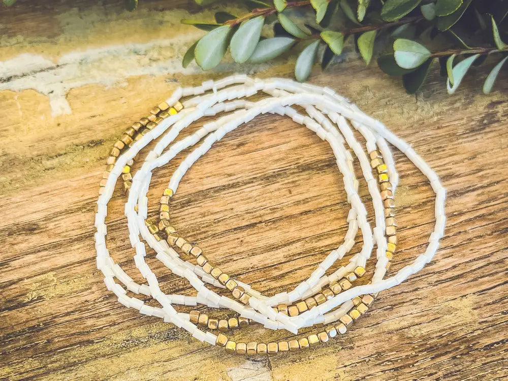 A delicate white and gold beaded multi strand stretch bracelet set featuring smooth cylindrical beads with metallic sheen