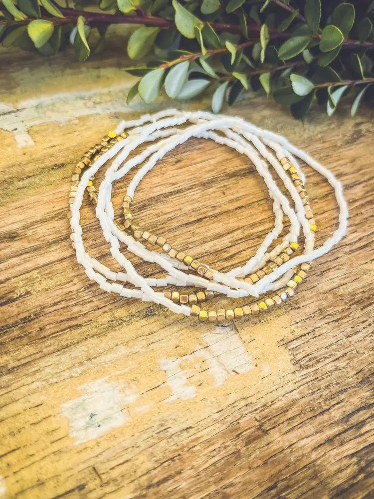 A white and gold beaded multi strand stacking bracelet set featuring delicate alternating beads in a coiled pattern