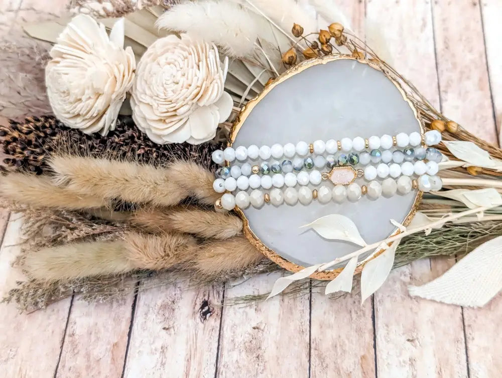 A delicate stack of white and light blue beaded bracelets with gold-toned accents displayed on a marble tray