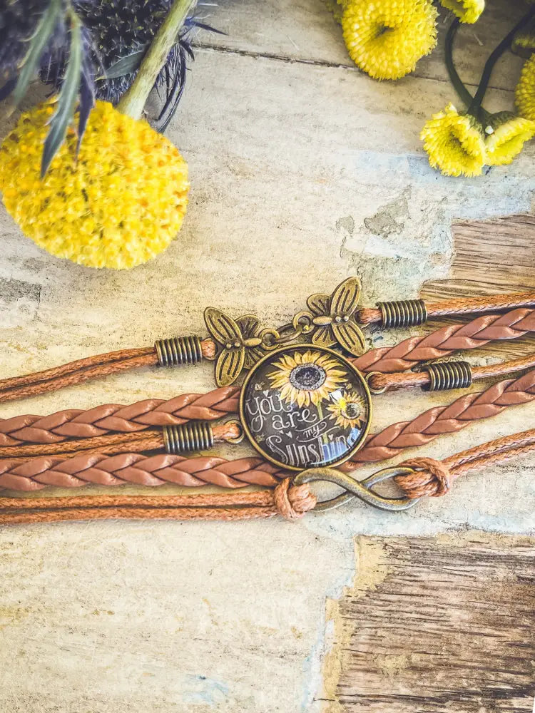 A rustic brown braided leather bracelet with a vintage brass butterfly charm and a sunflower glass cabochon