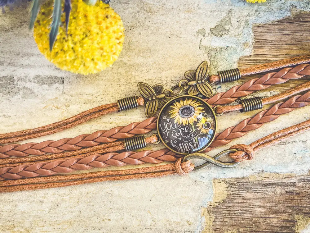 A rustic brown braided leather sunflower bracelet with a vintage brass butterfly charm and glass cabochon design