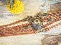 A rustic brown braided leather sunflower bracelet with a vintage brass butterfly charm and glass cabochon design