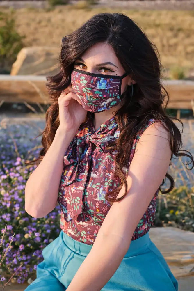 A model wearing a colorful beauty and the beast reversible cotton face mask with castles and fairytale illustrations