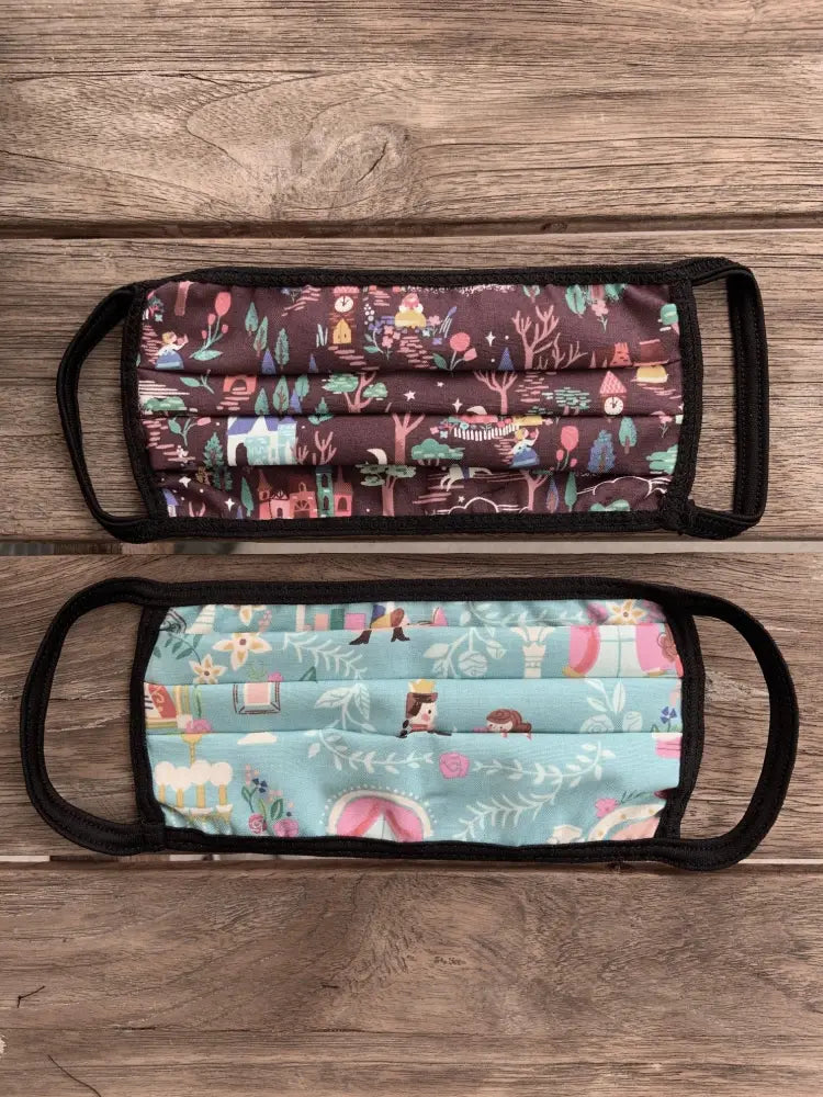 Two reversible cotton beauty and the beast face masks with black elastic loops featuring forest and fairy tale prints
