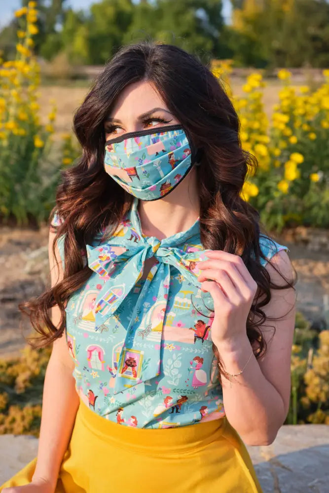A woman wearing a turquoise cotton reversible Beauty and the Beast face mask with playful cartoon print outdoors