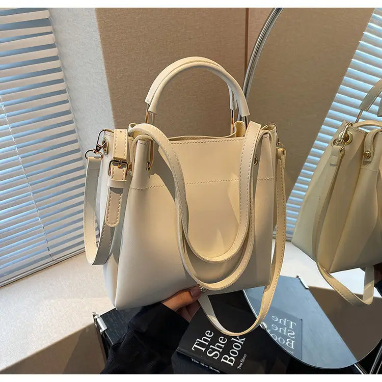 Cream-colored minimalist leather bucket bag with top handle and detachable shoulder strap.