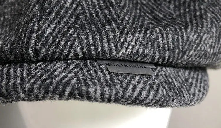 A gray herringbone woolen octagonal flat cap featuring subtle texture and a small made in china label stitched into the fold.