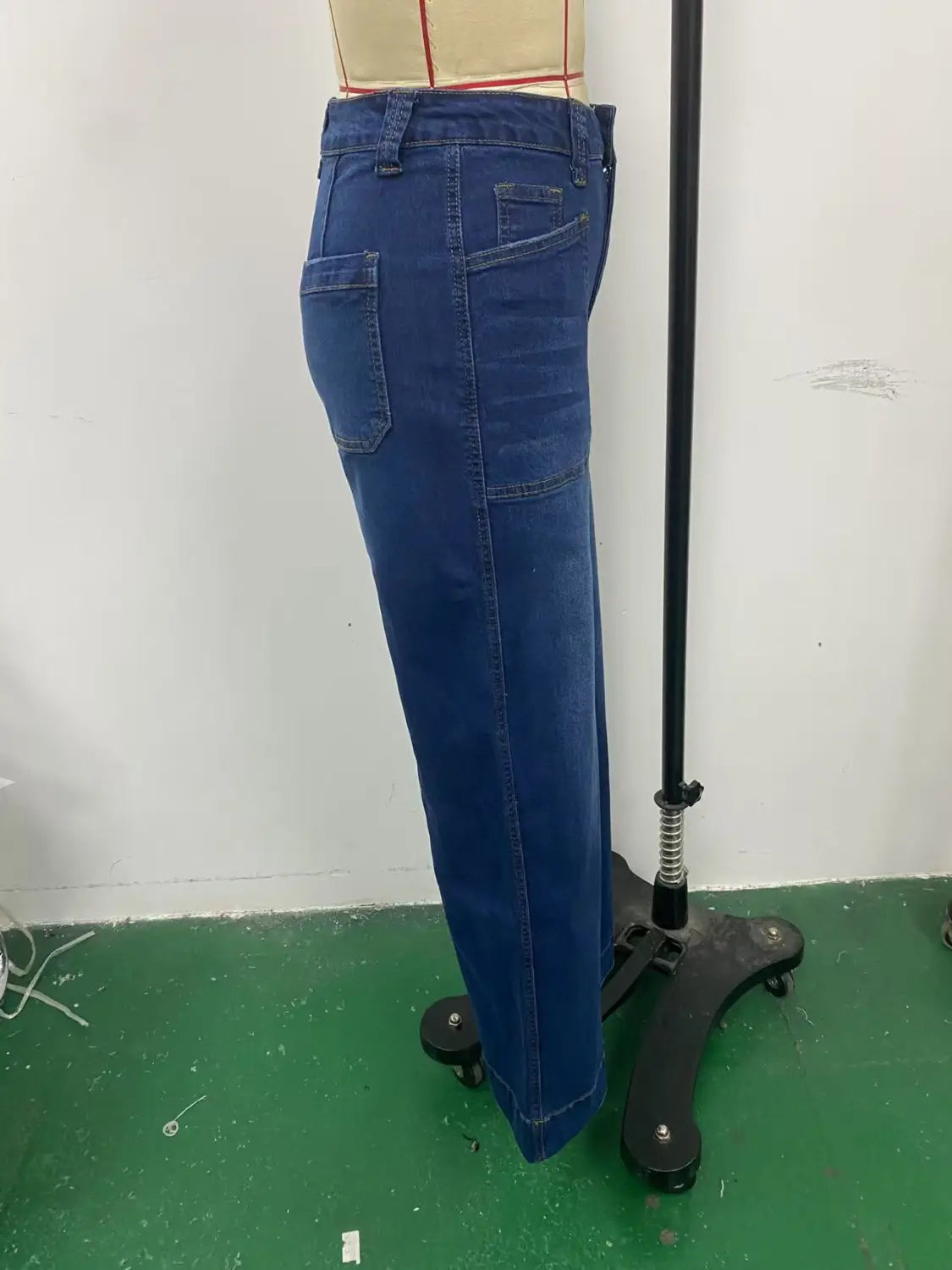 The image shows the back side of blue denim wide leg pants with a belt featuring a straight-leg cut and back pockets displayed on a mannequin.