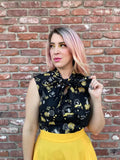 Black sleeveless 1950s cotton blouse with gold and white bee and floral patterns and bow neckline