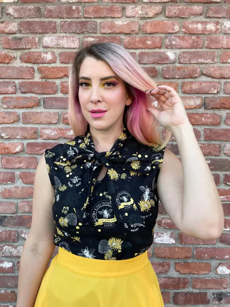 Black sleeveless 1950s cotton blouse with yellow and white bee print and bow neckline for a vintage look