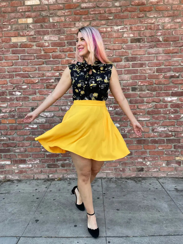 A vibrant yellow a-line skirt with high waist and flowing fabric paired with bee kind yellow floral bow neck 1950s cotton blouse