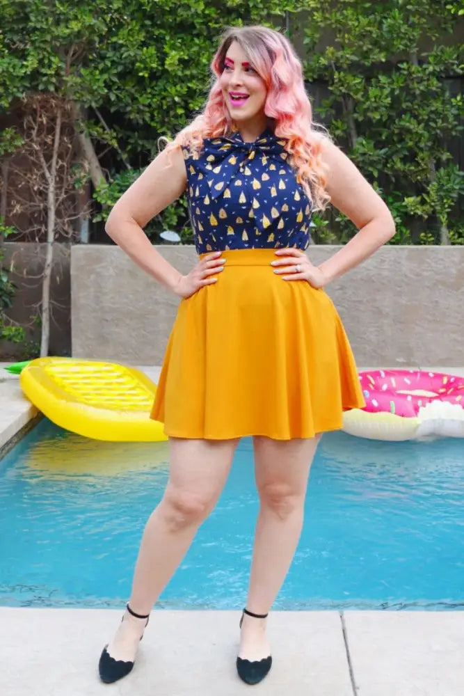 A vibrant yellow pleated skirt with a high waistband paired with a vintage beehive print bow neck sleeveless cotton blouse