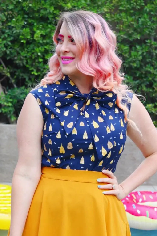 A navy blue sleeveless cotton blouse with a vintage beehive yellow pear print and bow neckline detail