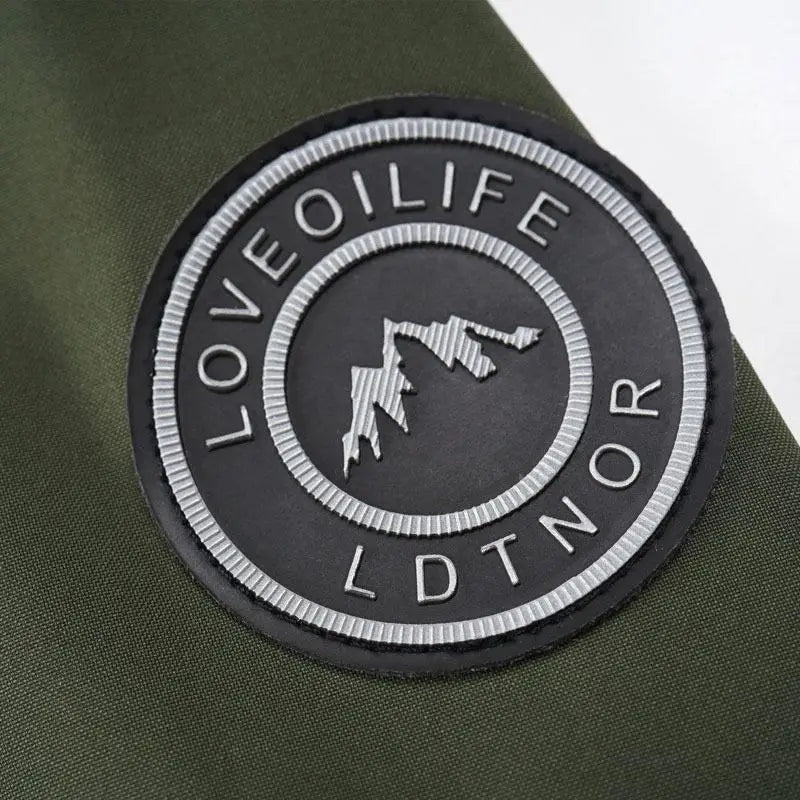 black circular patch with silver lettering and mountain silhouette stitched on the back side of an olive green mens outdoor fleece hooded jacket casual shell coat.