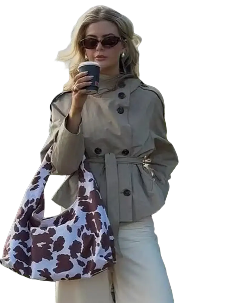 Beige double breasted trench coat paired with a white and brown cow print soft slouchy hobo bag