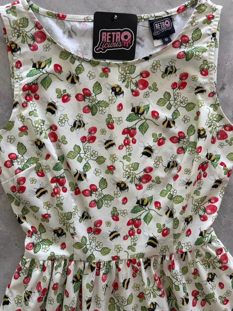 A sleeveless white 1950s vintage cotton dress with pockets featuring a red strawberry and bee pattern