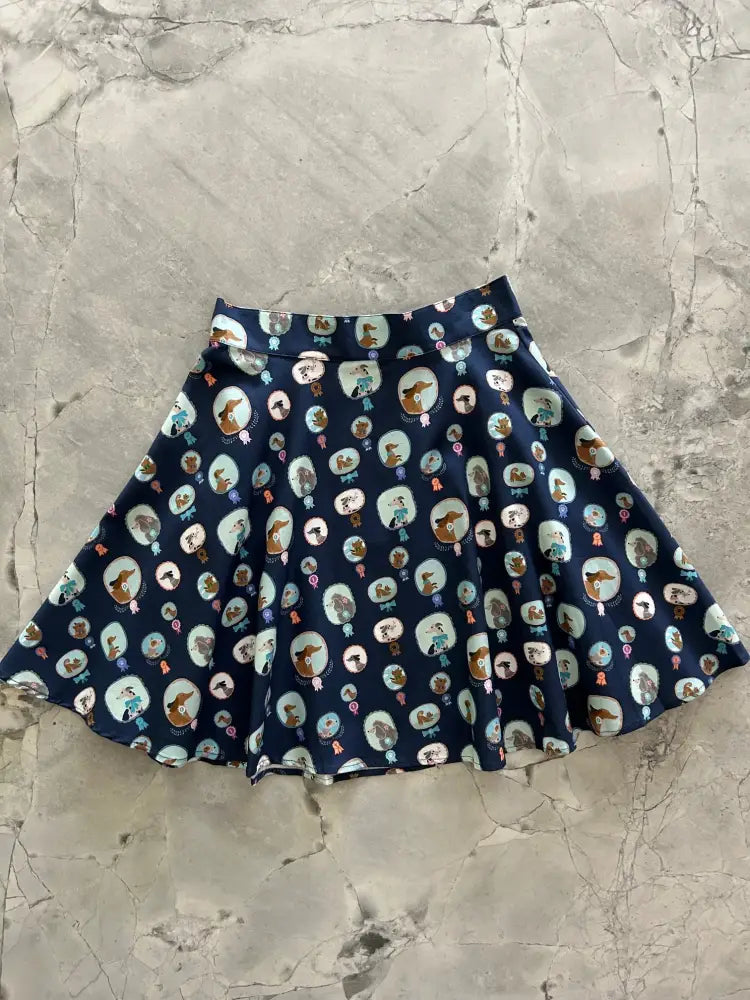 A navy blue pleated skater skirt with a playful cartoon dog print in oval frames and subtle pastel accents