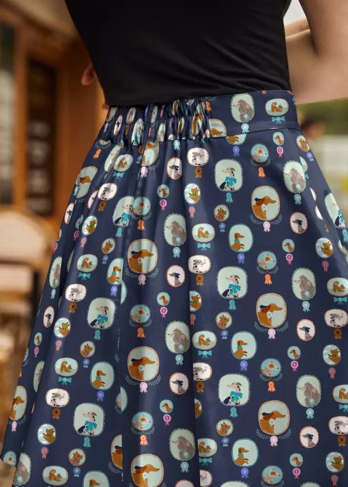 A navy blue Best in Show dog print pleated skater skirt with a playful cartoon dog pattern and colorful ribbons