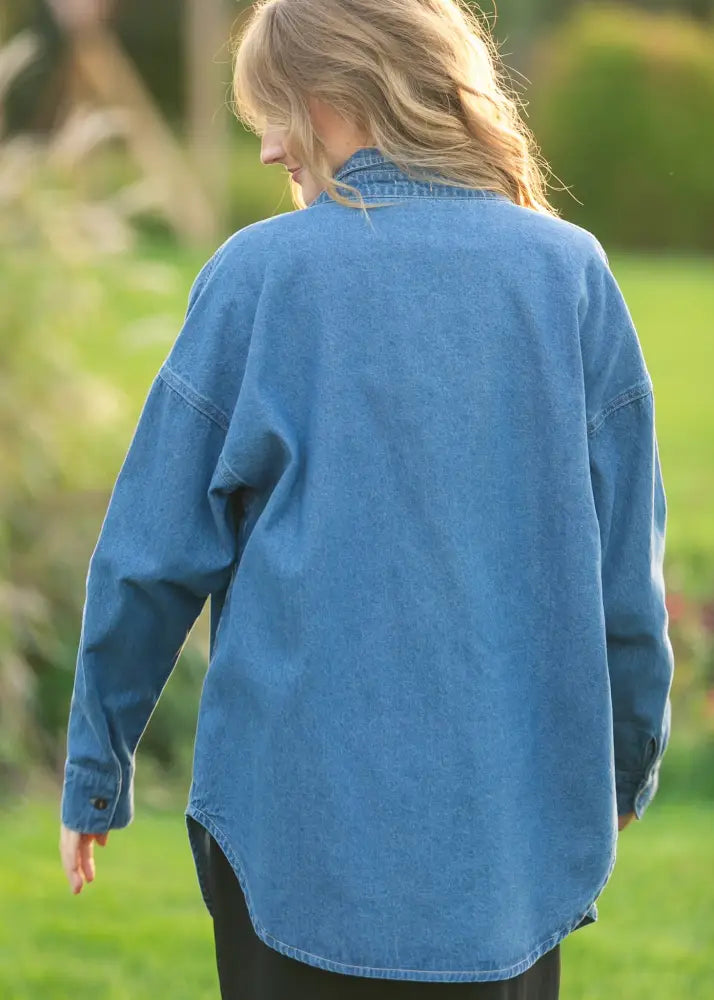 Betty denim relaxed button up shirt is a medium-wash blue cotton denim with a relaxed fit, classic collar, and buttoned cuffs