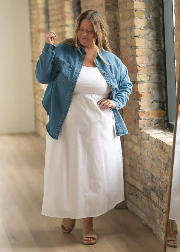 White cotton midi dress with fitted bodice and flowing skirt worn under oversized Betty denim relaxed button up shirt