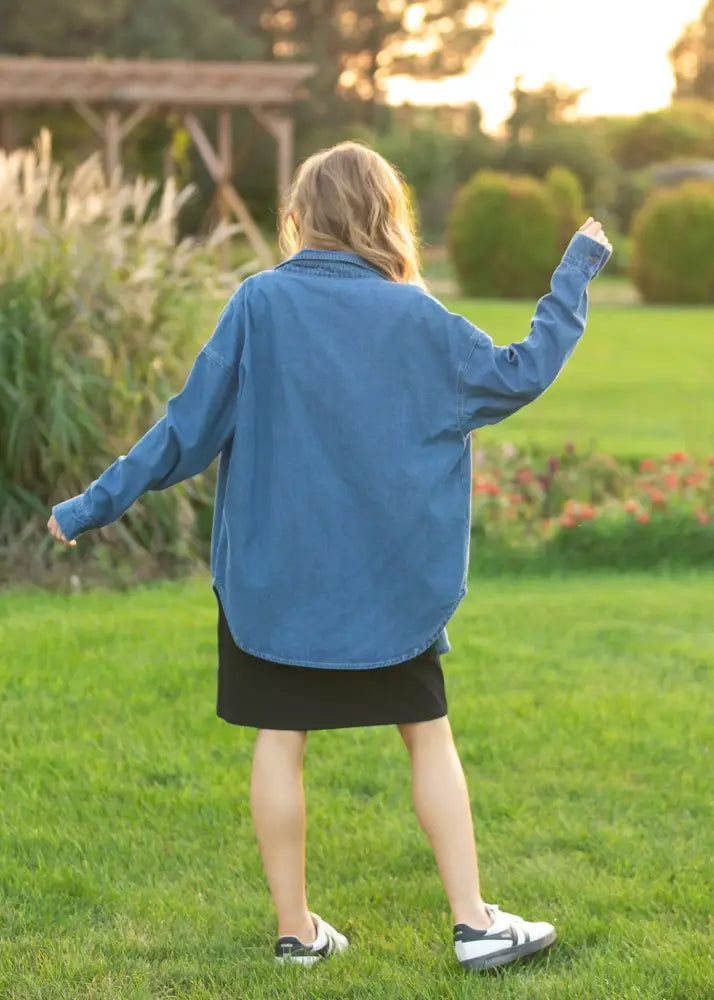 A woman wearing a betty denim relaxed button up shirt in medium blue loose fitting denim with long sleeves
