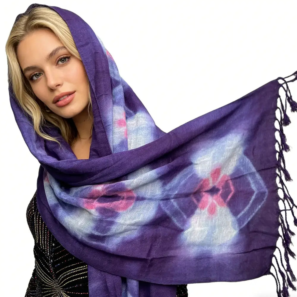 Un foulard en viscose bohème floral violet, présentant un motif tie-dye violet avec des motifs floraux roses et blancs et des pompons noirs le long des bords.