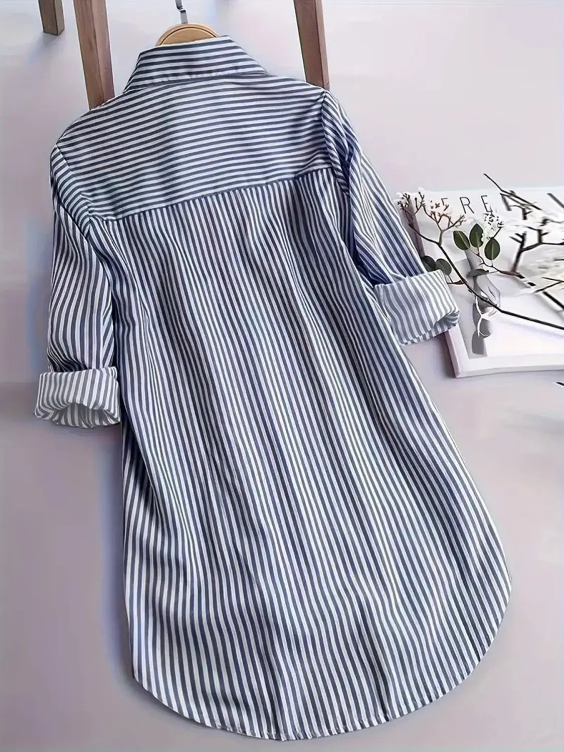Chemise boutonnée en coton à rayures verticales bleu marine et blanches, manches longues, suspendue à un cintre en bois, convient pour un usage décontracté.