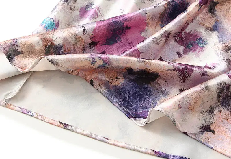 Floraler Satin-Midirock mit hoher Taille und einem fließenden Seidenschal mit sanftem Aquarell-Blumenmuster in Pink, Violett und gedämpftem Blau auf elfenbeifarbener Basis.