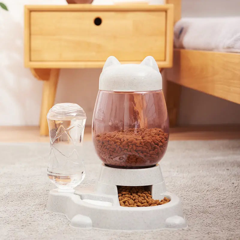 White cat-shaped automatic cat feeder and water fountain with a transparent pinkish bowl filled with kibble and a matching water dispenser for pet feeding.