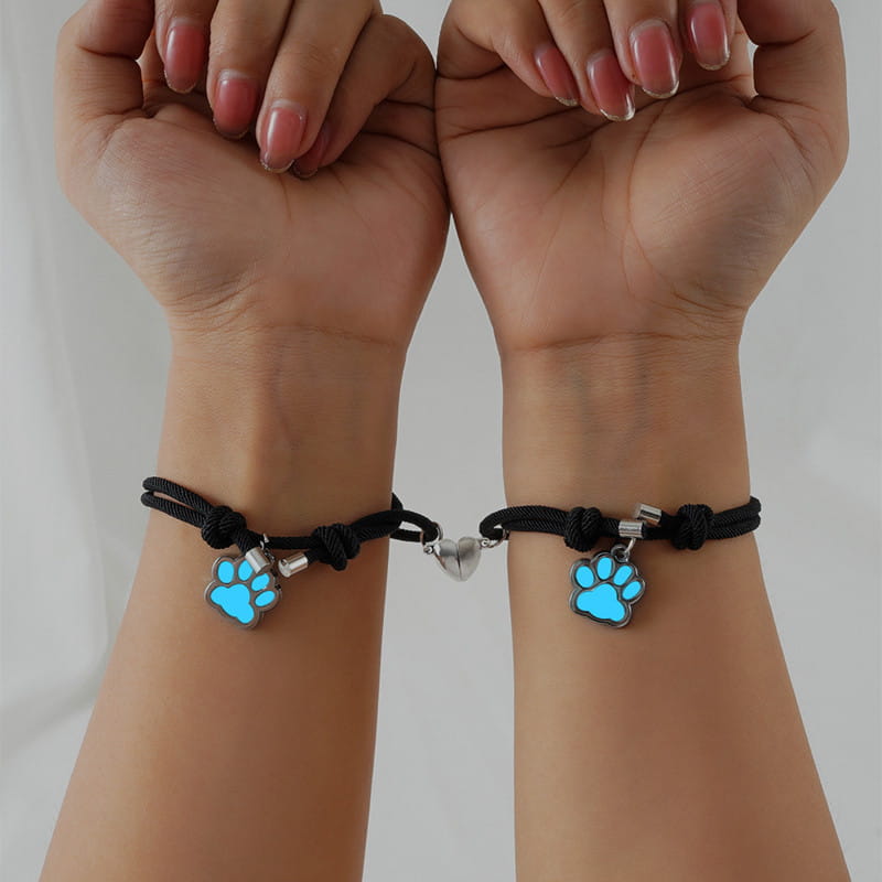 black cord couple bracelets featuring glowing blue paw print charms and a silver heart connector made with magnetic material