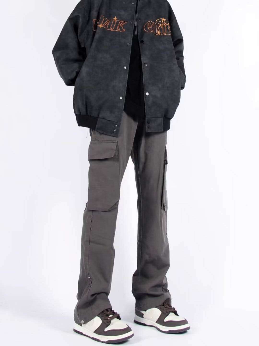 Chaqueta bomber negra con letras bordadas doradas y rojas en el pecho, combinada con pantalones cargo rectos de pierna recta con múltiples bolsillos.
